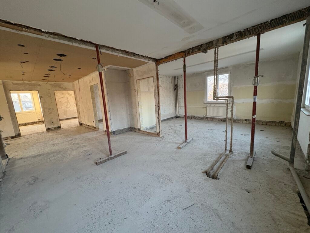Offener Innenraum im entkernten Bestandsgebäude mit freigelegten Decken, provisorischen Stützen und sichtbaren Leitungen während der Umbauphase.