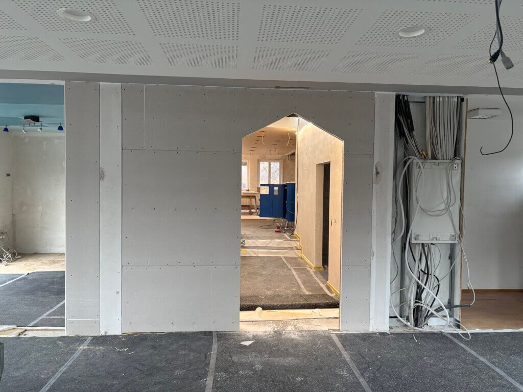 Neu errichtete Trockenbauwände mit Durchgang im Innenbereich, sichtbare Elektroverkabelung und abgehängte Akustikdecke im fortgeschrittenen Ausbauzustand.